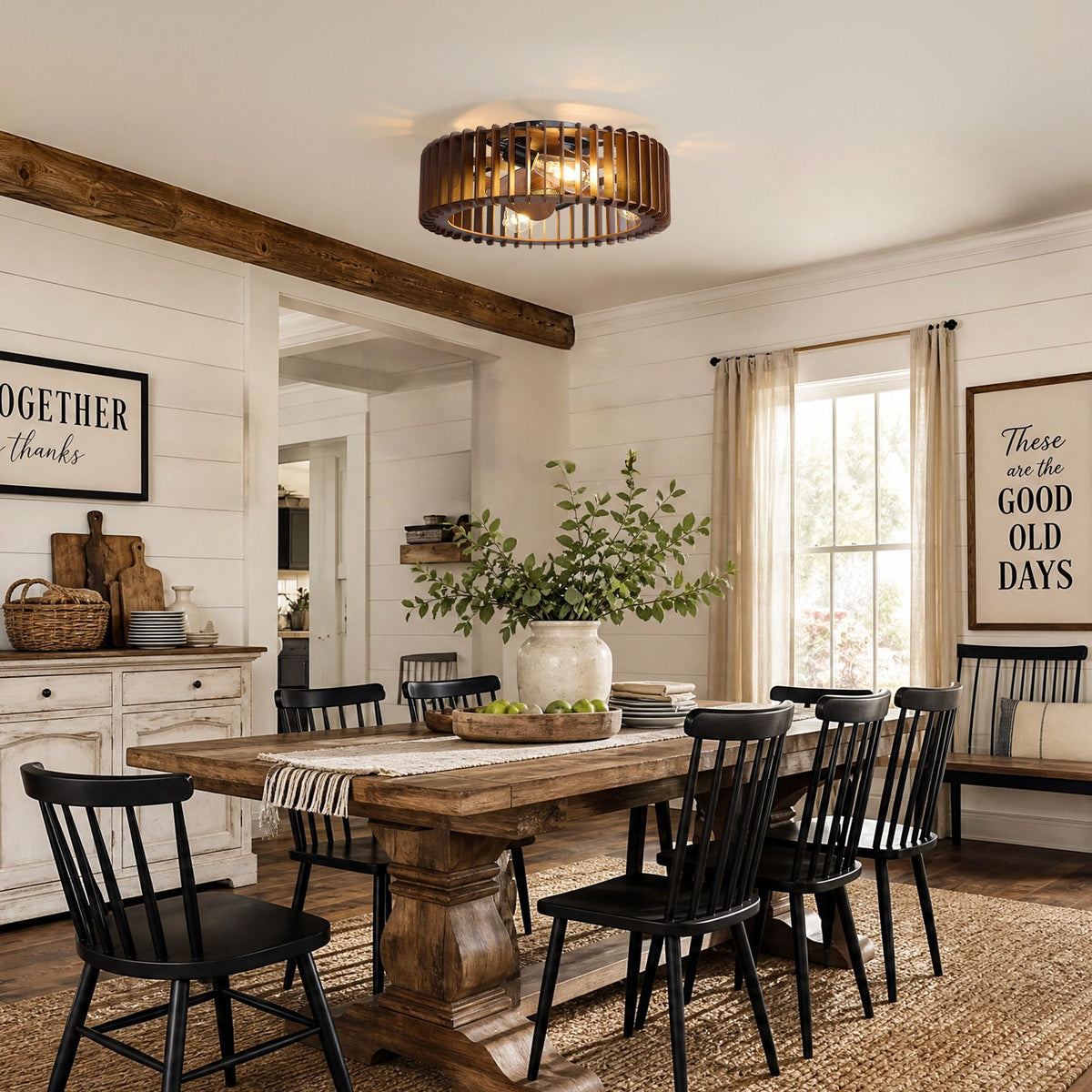 Industrial caged ceiling fan in farmhouse dining room — thick wood table, black Windsor chairs, decorative signs on shiplap walls, wood beam ceiling, warm Edison bulb glow | CARRA HOME