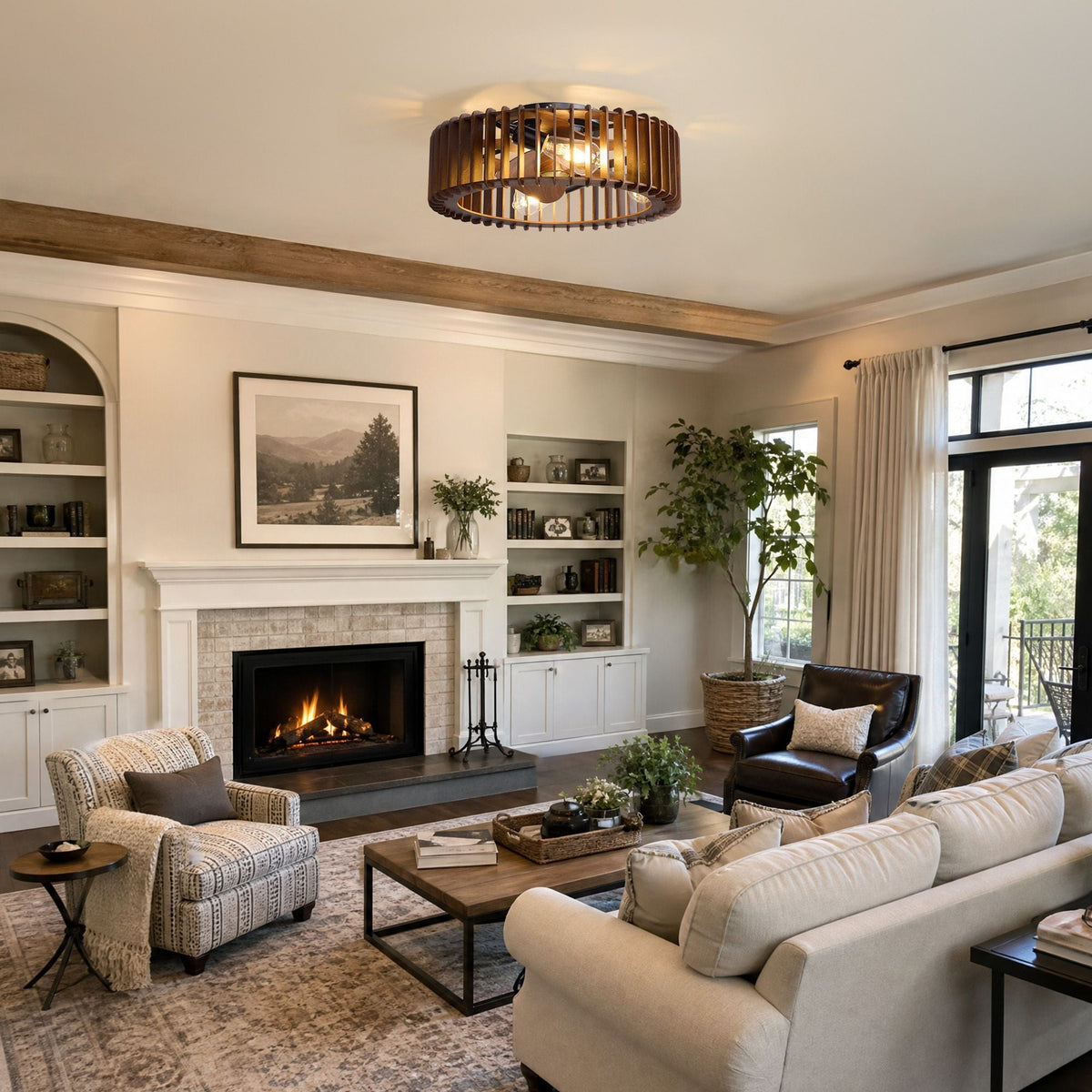 Industrial caged ceiling fan in farmhouse living room — beige sofa, patterned armchair, dark leather chair, lit fireplace, bookshelves, wood beam ceiling, vintage rug | CARRA HOME