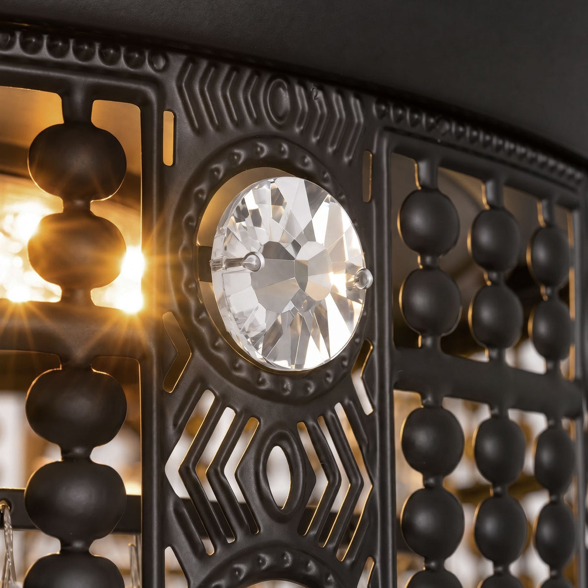 Close-up of ceiling fan canopy and LED light — black ornate metalwork with geometric cutouts, central crystal jewel, beaded crystal trim, warm LED starburst glow | CARRA HOME