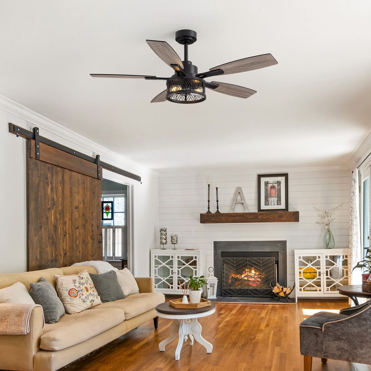 Farmhouse ceiling fan in rustic living room — sliding barn door, shiplap walls, fireplace, beige sofa, wood flooring, cozy farmhouse decor | CARRA HOME