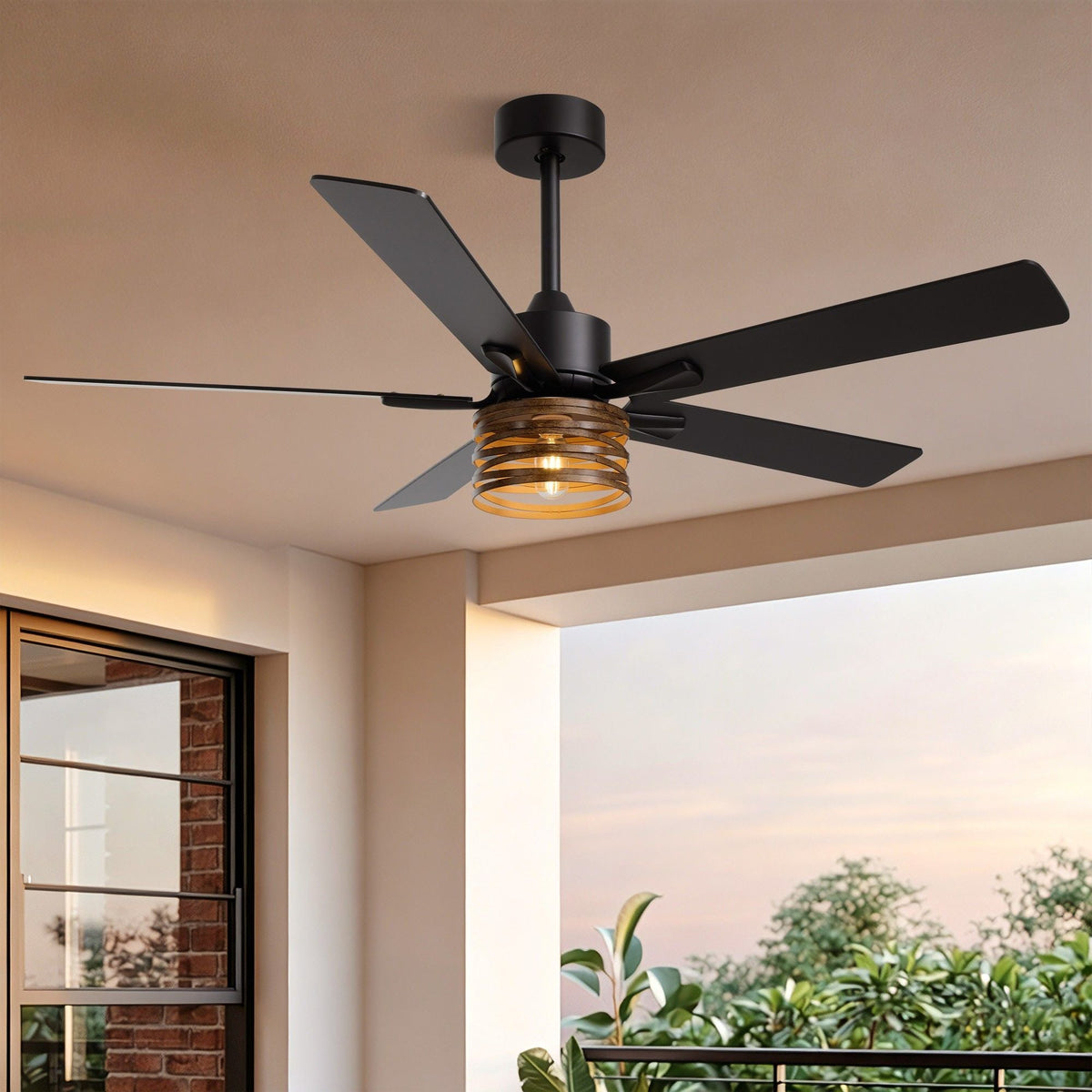 52" Industrial Farmhouse Ceiling Fan with Light — matte black motor, wood grain blades, amber ribbed glass light shade, mounted on patio ceiling with brick wall and garden view | CARRA HOME