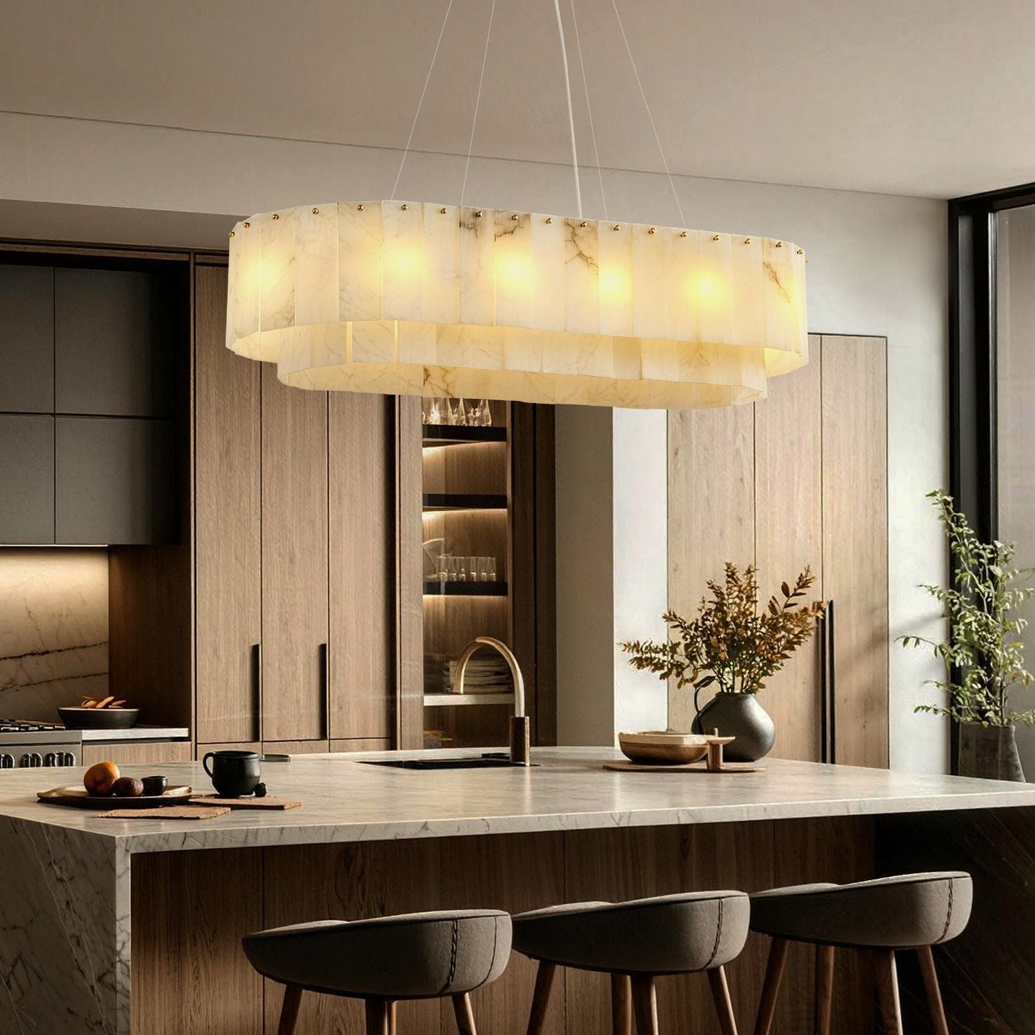 Aethel Modern Natural Alabaster Linear Chandelier in a modern kitchen — hanging above a marble kitchen island with wooden bar stools, pendant lights illuminating the workspace with cabinets and appliances in the background -carra-home