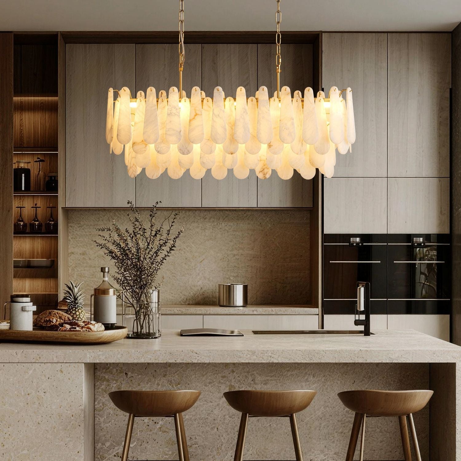 Apex Modern Minimalist Alabaster Linear Chandelier hanging above a modern kitchen island — paired with light wood cabinetry, marble countertop, and minimalist decor including a pineapple and glass vases -carra-home