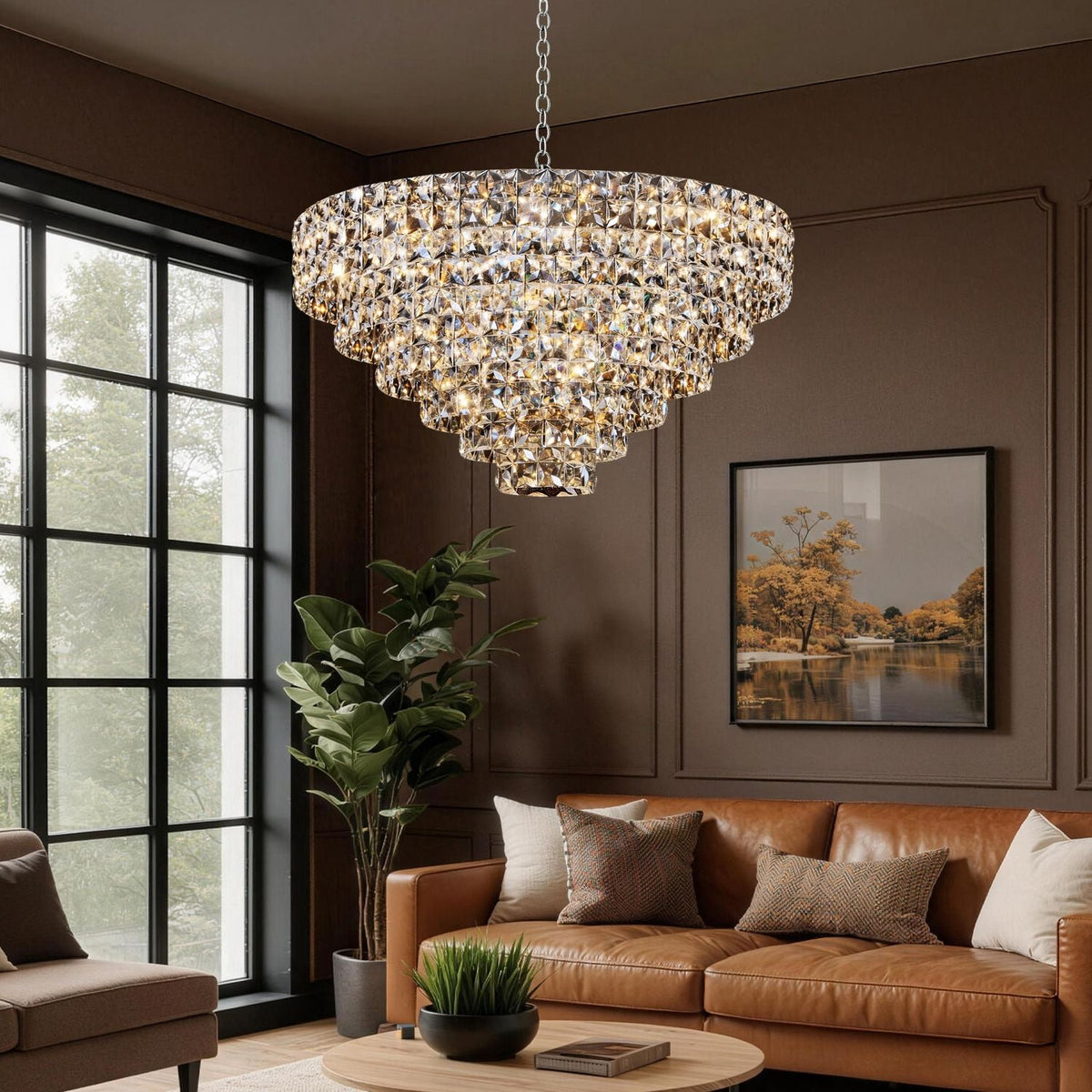 Aria Modern Gold K9 Crystal Glacier Chandelier in a cozy living room — casting layered, ambient light over a tan leather sofa, large windows, and lush greenery for modern luxury | Carra Home