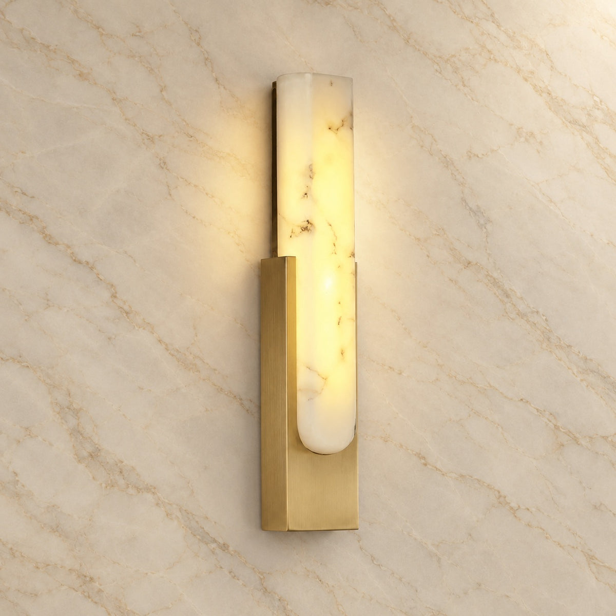 Emilia Alabaster Wall Sconce with gold hardware, illuminated, on a marble wall | CARRA HOME