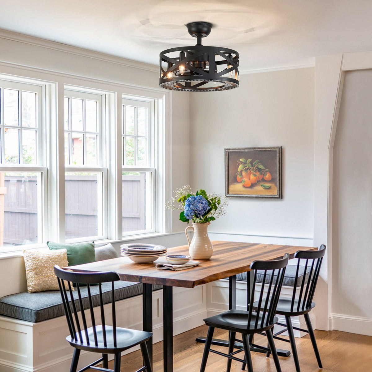 Caged ceiling fan in breakfast nook/dining area — wooden table, black spindle chairs, bay window seat, fruit wall art | CARRA HOME