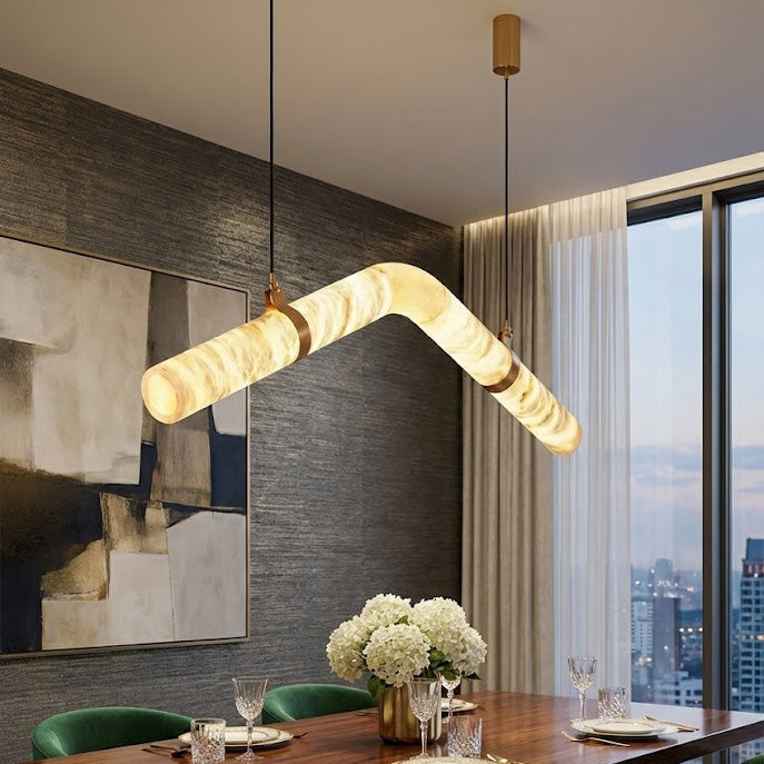 Curved alabaster tube chandelier above a dining table with green chairs | CARRA HOME