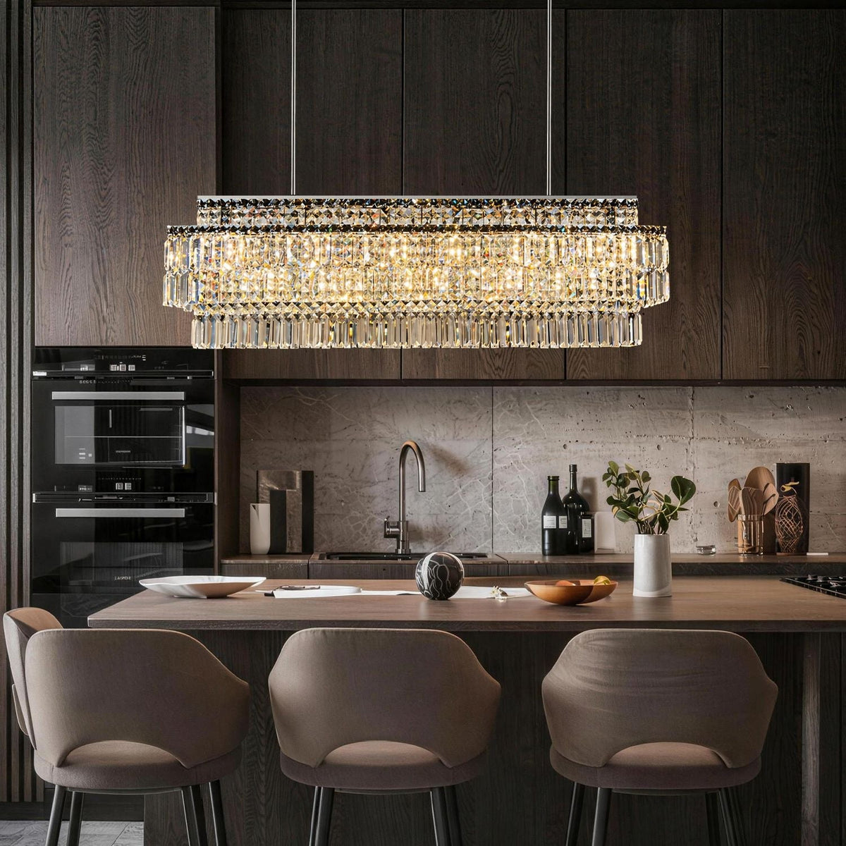Stellar Grand Linear Silver Multi-Faceted K9 Crystal Chandelier in a kitchen island — suspended above a wooden countertop with dark cabinets, a marble backsplash, and kitchen utensils | Carra Home