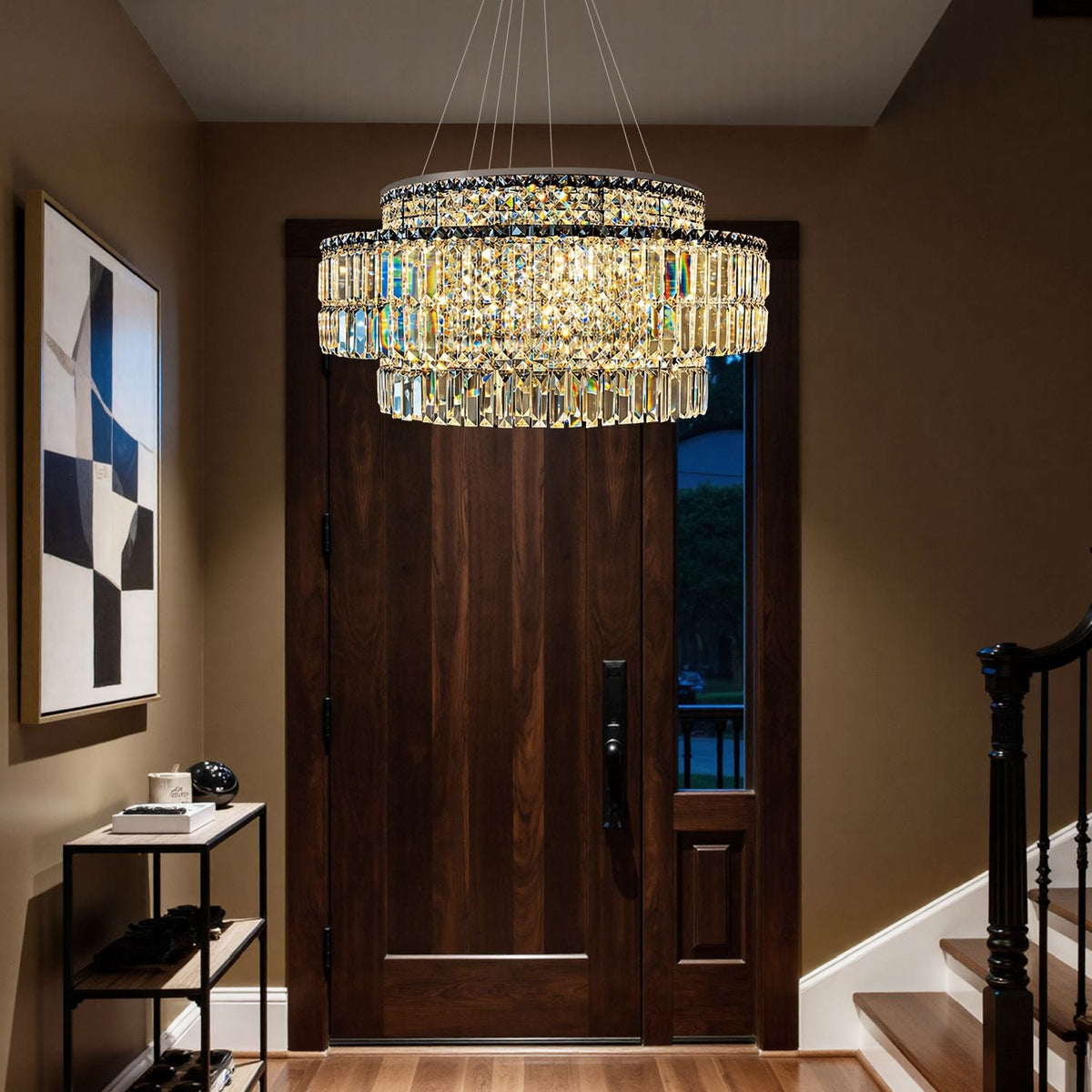 Stellar Modern Silver Multi-Faceted K9 Crystal Round Chandelier in a foyer — suspended above a console table with decor, books, and a dark paneled wall with a modern art piece | Carra Home