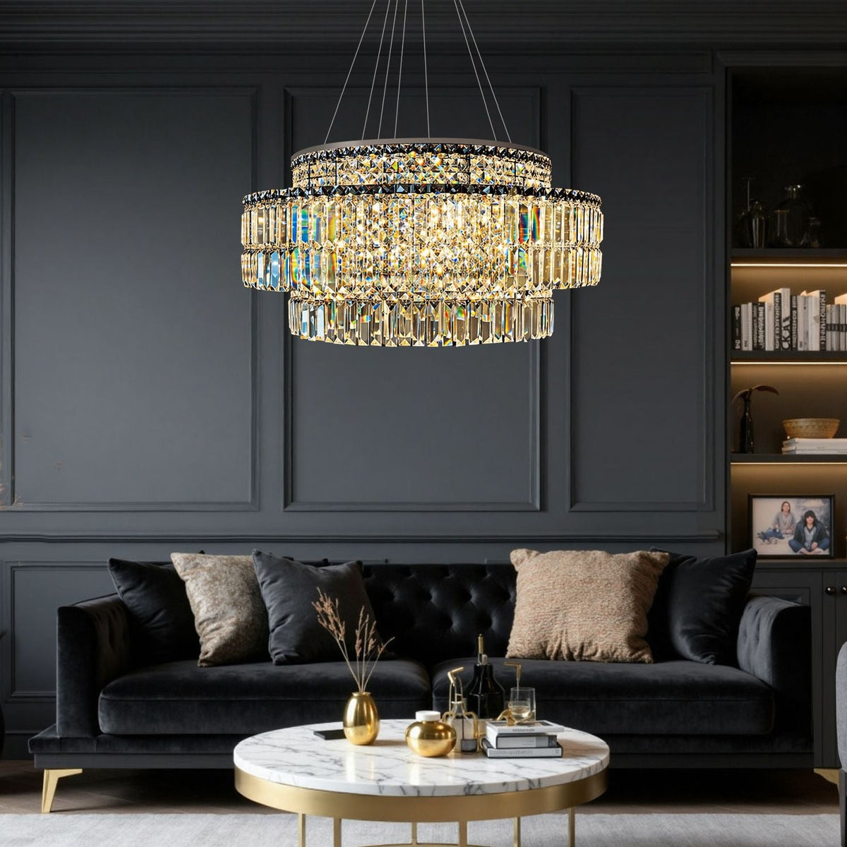 Stellar Modern Silver Multi-Faceted K9 Crystal Round Chandelier in a living room — suspended above a black velvet sofa with decorative pillows, a marble coffee table, and dark paneled walls | Carra Home