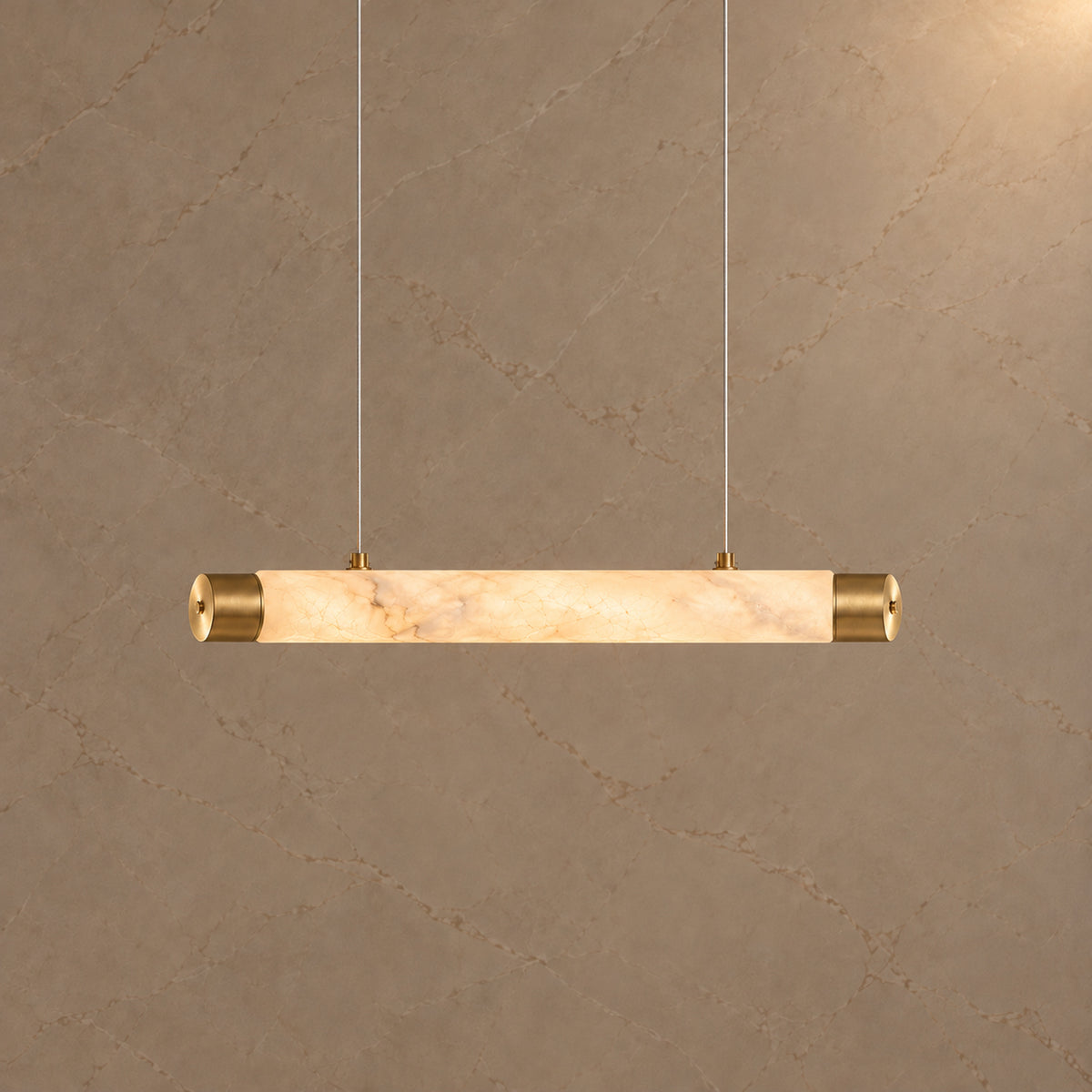 Virel Alabaster Linear Chandelier — Gold 100 cm alabaster tube chandelier illuminated at 3000K against a marble wall | CARRA HOME