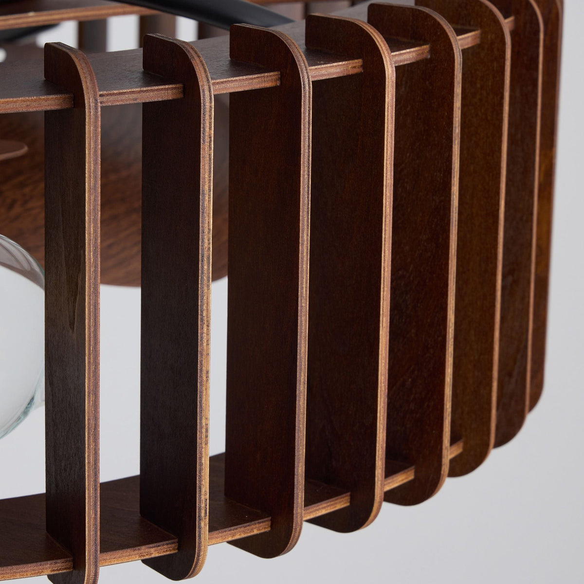 Close-up of industrial caged fan wooden slat structure — dark wood vertical bars, curved top and bottom rails, layered plywood edge grain, flush mount ceiling plate detail | CARRA HOME
