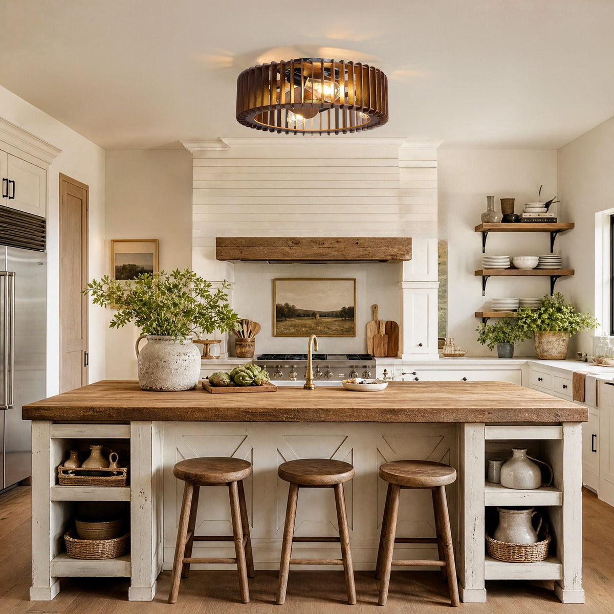 Industrial caged ceiling fan over farmhouse kitchen island — wood countertop, black stools, white shiplap walls, open shelving with dishes and plants, pendant warm light | CARRA HOME
