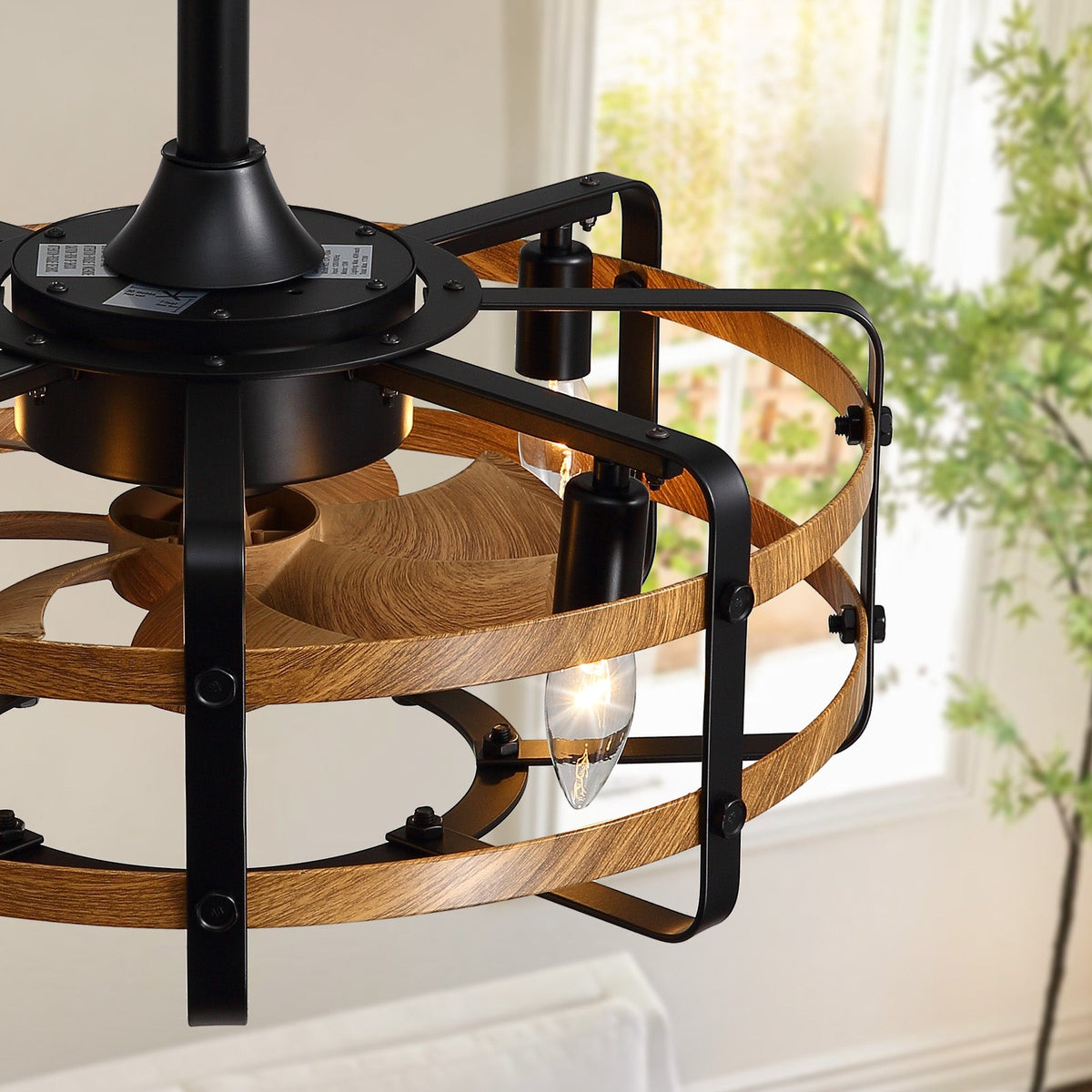 Close-up of caged ceiling fan structure — black metal brackets with screws, wood grain curved slats, vintage bulb, downrod mount, craftsmanship detail, window with greenery background | CARRA HOME
