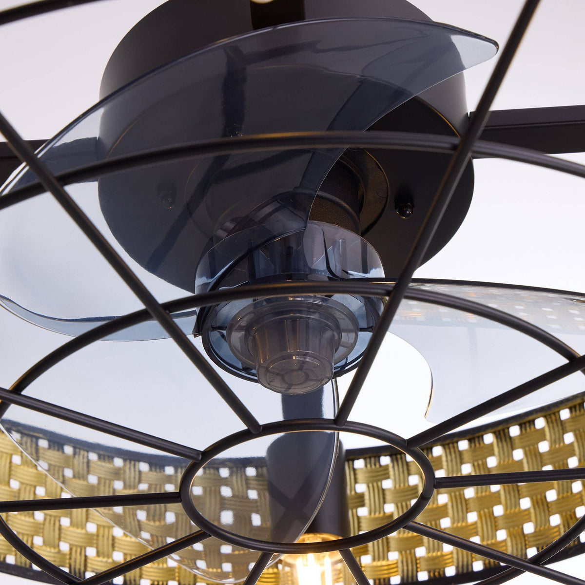 Close-up of boho rattan ceiling fan blades and motor — translucent enclosed blades, matte black motor housing, wire cage, vintage Edison bulb glow, woven rattan shade | CARRA HOME