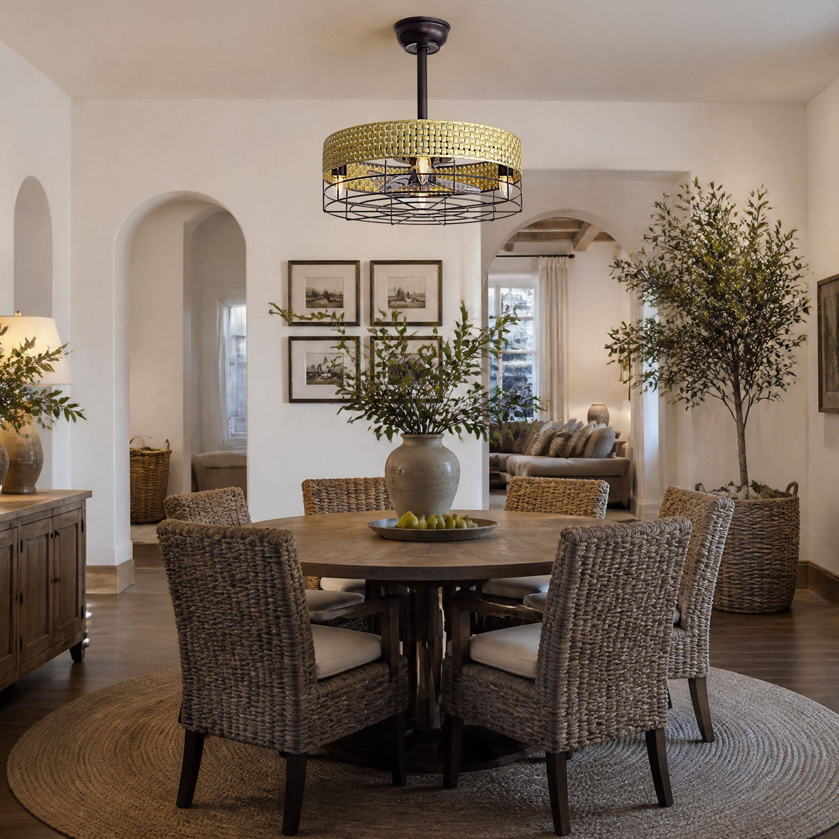 Rattan caged fan in dining room — round wood table, woven chairs, arched entryways, olive tree, neutral boho interior | CARRA HOME