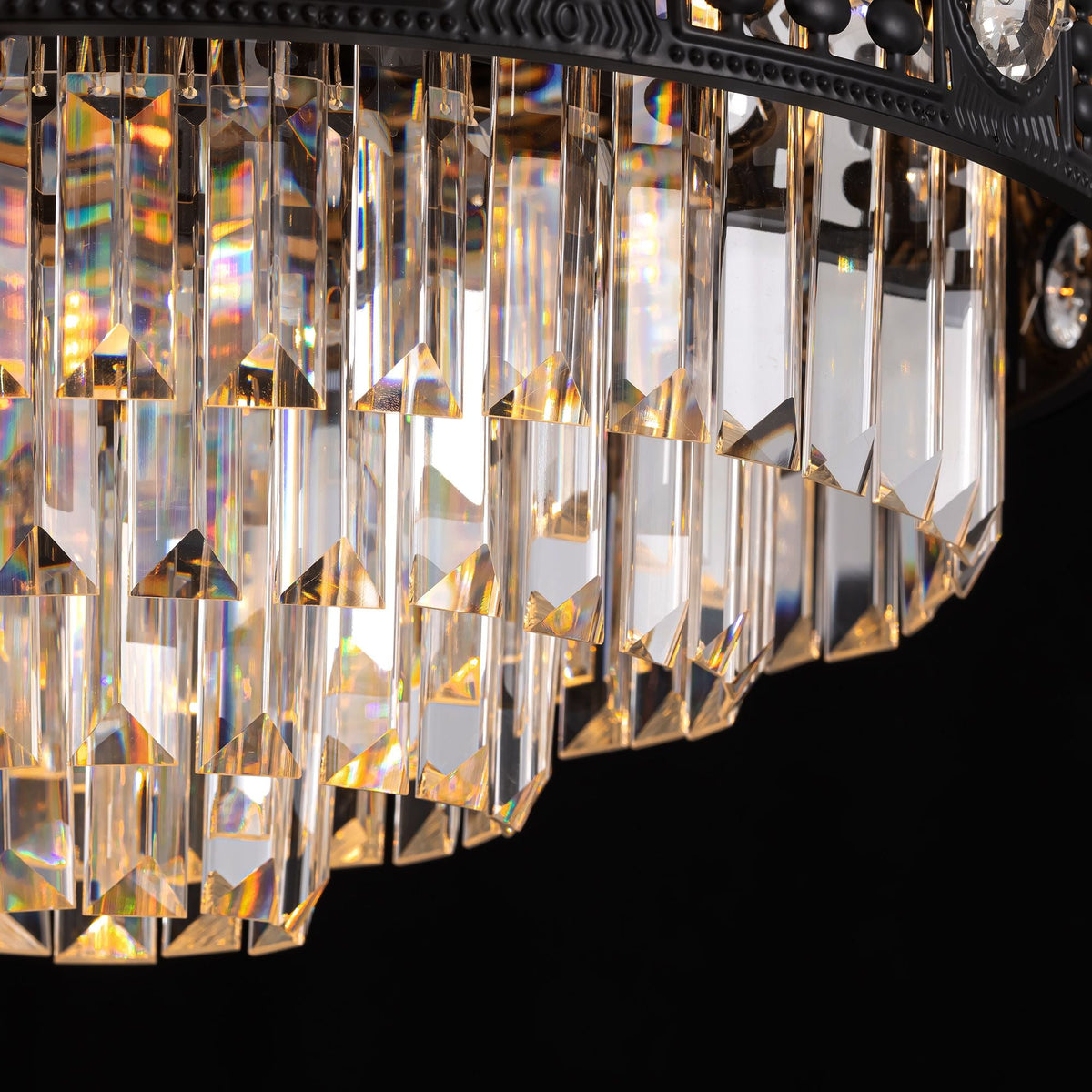 Close-up of black crystal ceiling fan — tiered rectangular and faceted crystal pendants, light refraction with golden and rainbow reflections, black metal frame, dark background | CARRA HOME