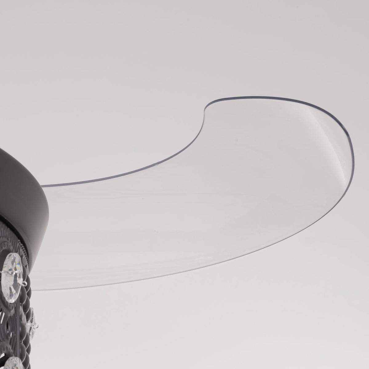 Close-up of retractable fan blade — transparent curved acrylic blade with dark edge trim, extended from black center hub, invisible blade design detail | CARRA HOME