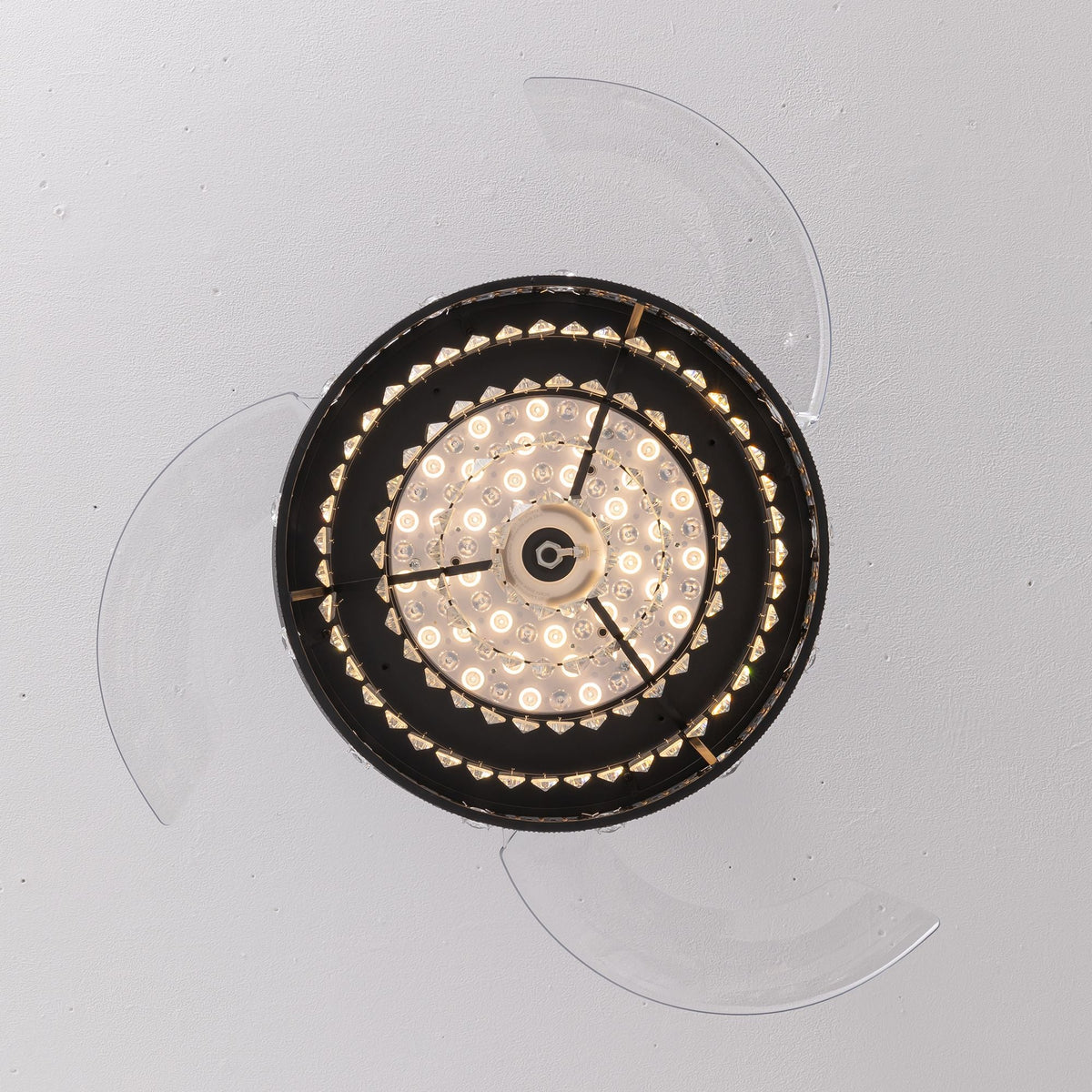 Top-down view of 48" black crystal retractable ceiling fan — transparent blades fully extended, central LED light ring, black radial frame, flush mount to ceiling | CARRA HOME