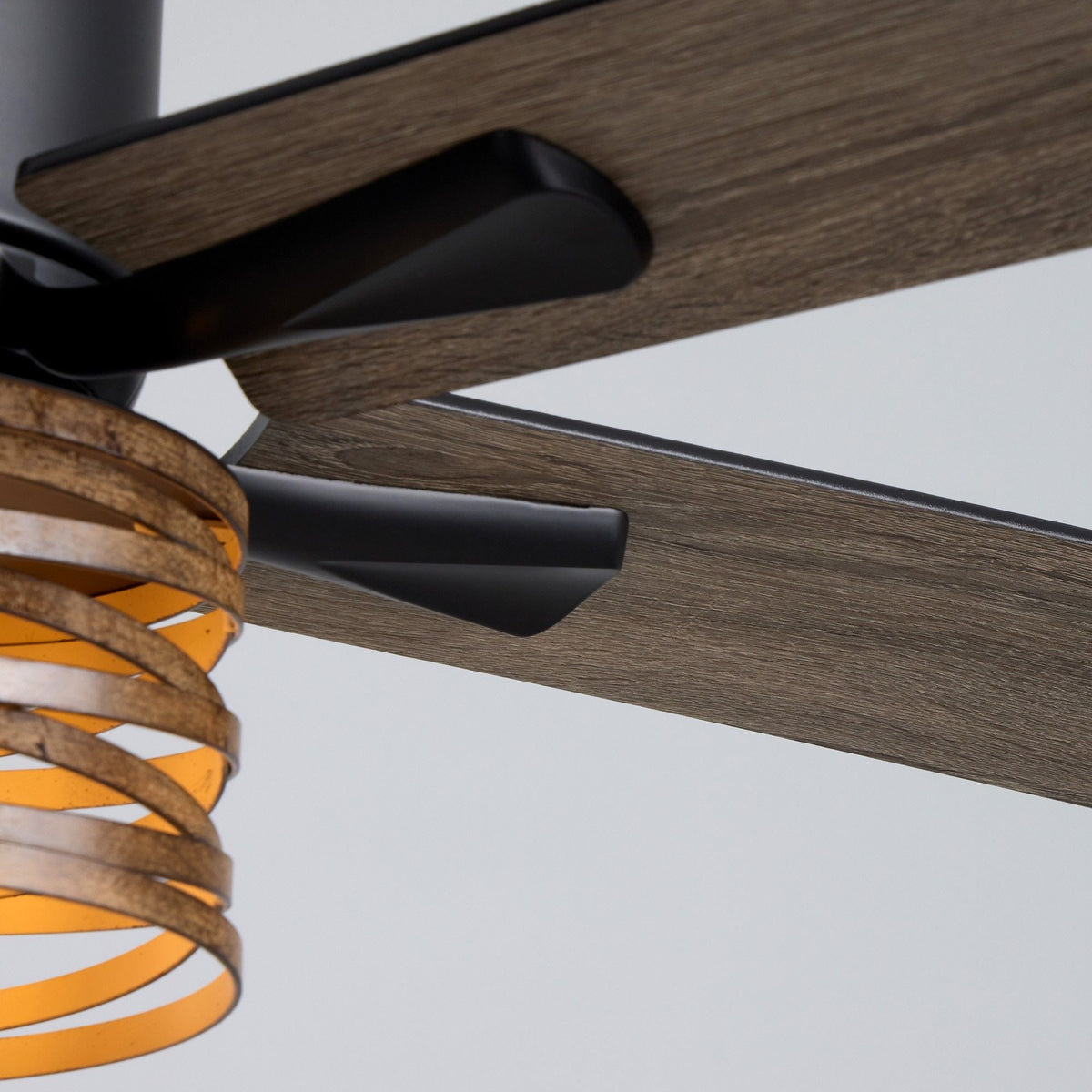 Close-up of 52" industrial farmhouse ceiling fan — wood grain reversible blade with black bracket and motor arm, amber ribbed glass light shade edge, matte black hardware, craftsmanship detail | CARRA HOME