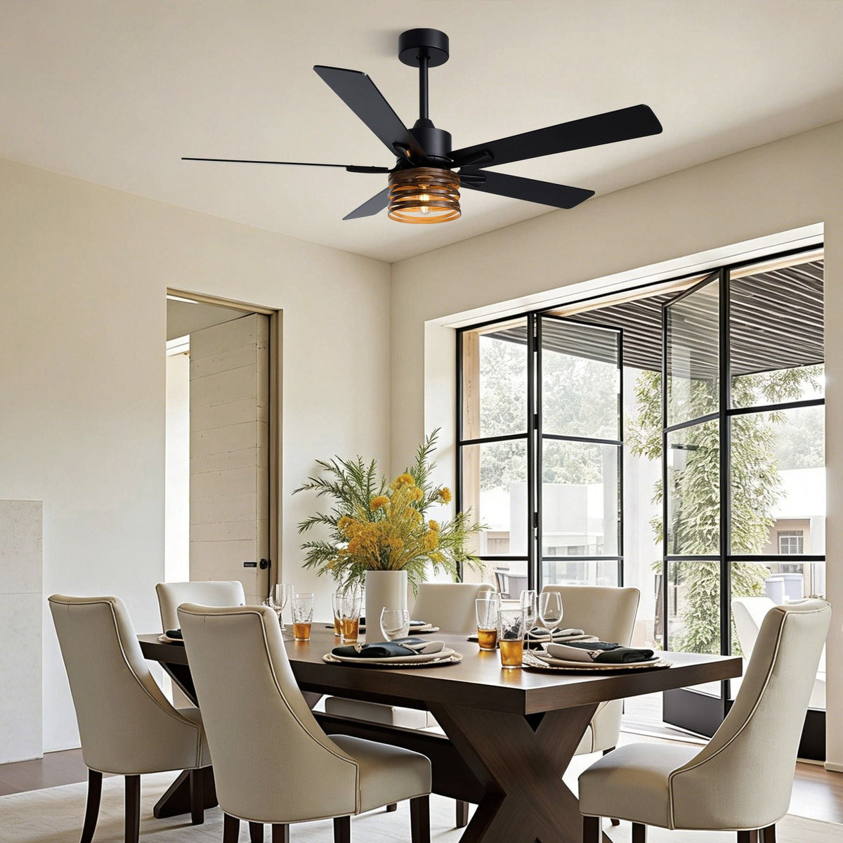 Industrial farmhouse ceiling fan in dining room — dark wood table, cream upholstered chairs, amber glass light shade, black frame folding glass doors, floral centerpiece | CARRA HOME