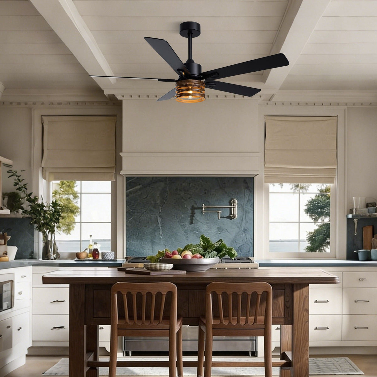 Industrial farmhouse ceiling fan over kitchen island — white cabinets, dark countertop, wood stools, windows with garden view, fruit bowl on counter | CARRA HOME