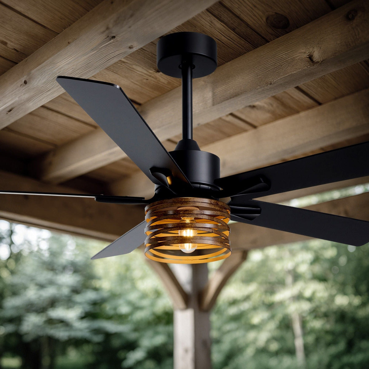 Industrial farmhouse ceiling fan outdoor patio — wood plank ceiling, black metal frame, amber glass light shade, lush green garden background, warm glow | CARRA HOME