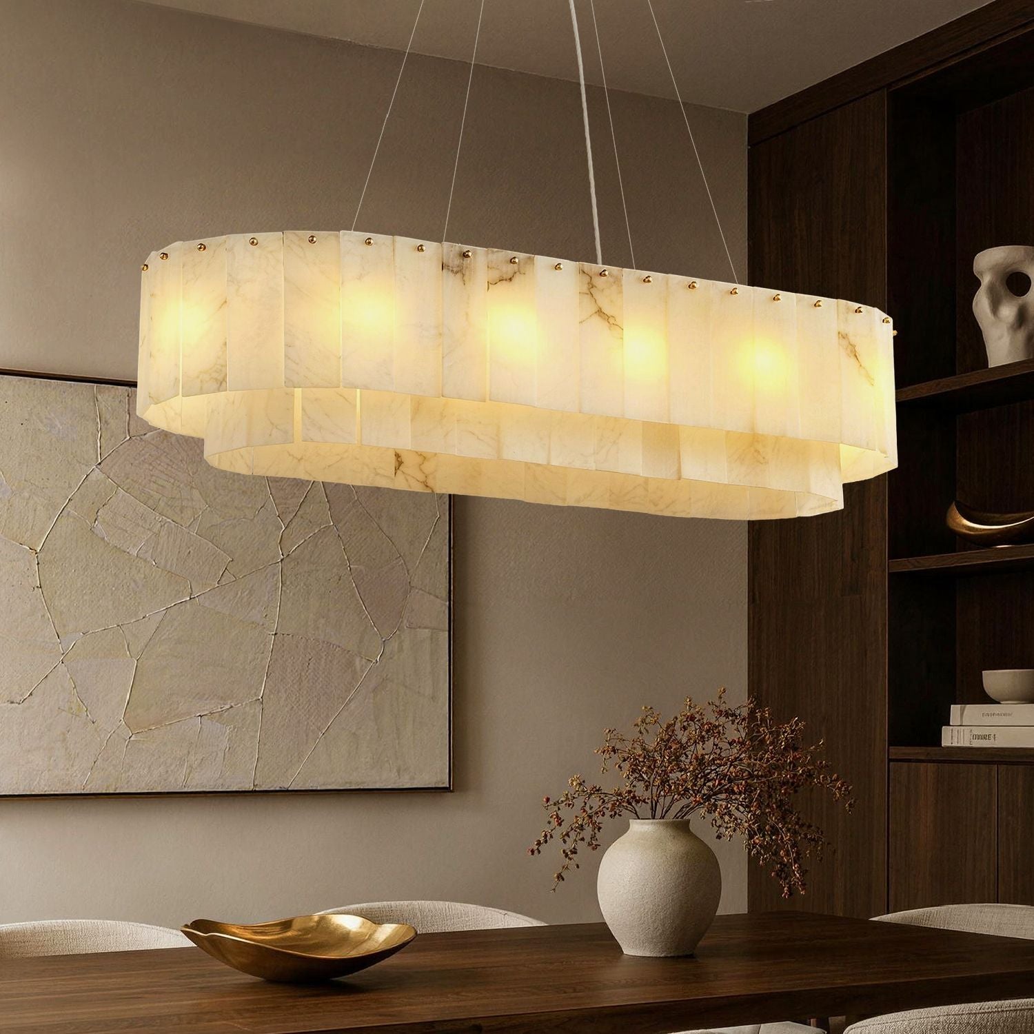 Aethel Modern Natural Alabaster Linear Chandelier in a dining room — featuring a tiered oval design with natural alabaster stone tiles, illuminated above a wooden dining table with elegant place settings and a dark wood cabinet in the background -carra-home