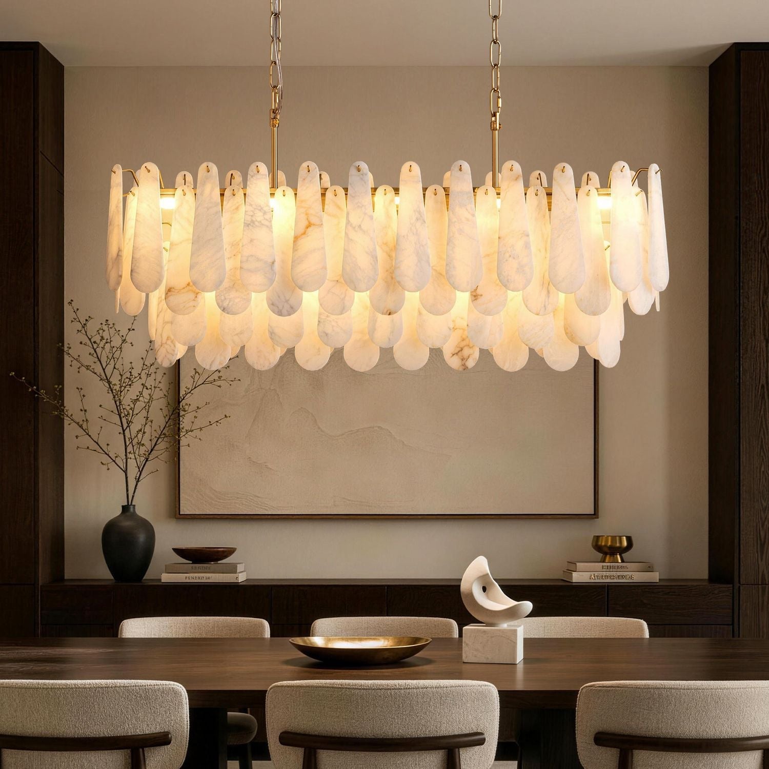 Apex Modern Minimalist Alabaster Linear Chandelier in a sophisticated dining room — featuring a rectangular frame with layered alabaster stone pendants, suspended above a dark wood table set with a golden bowl and a vase of white flowers, against a beige wall with abstract art -carra-home