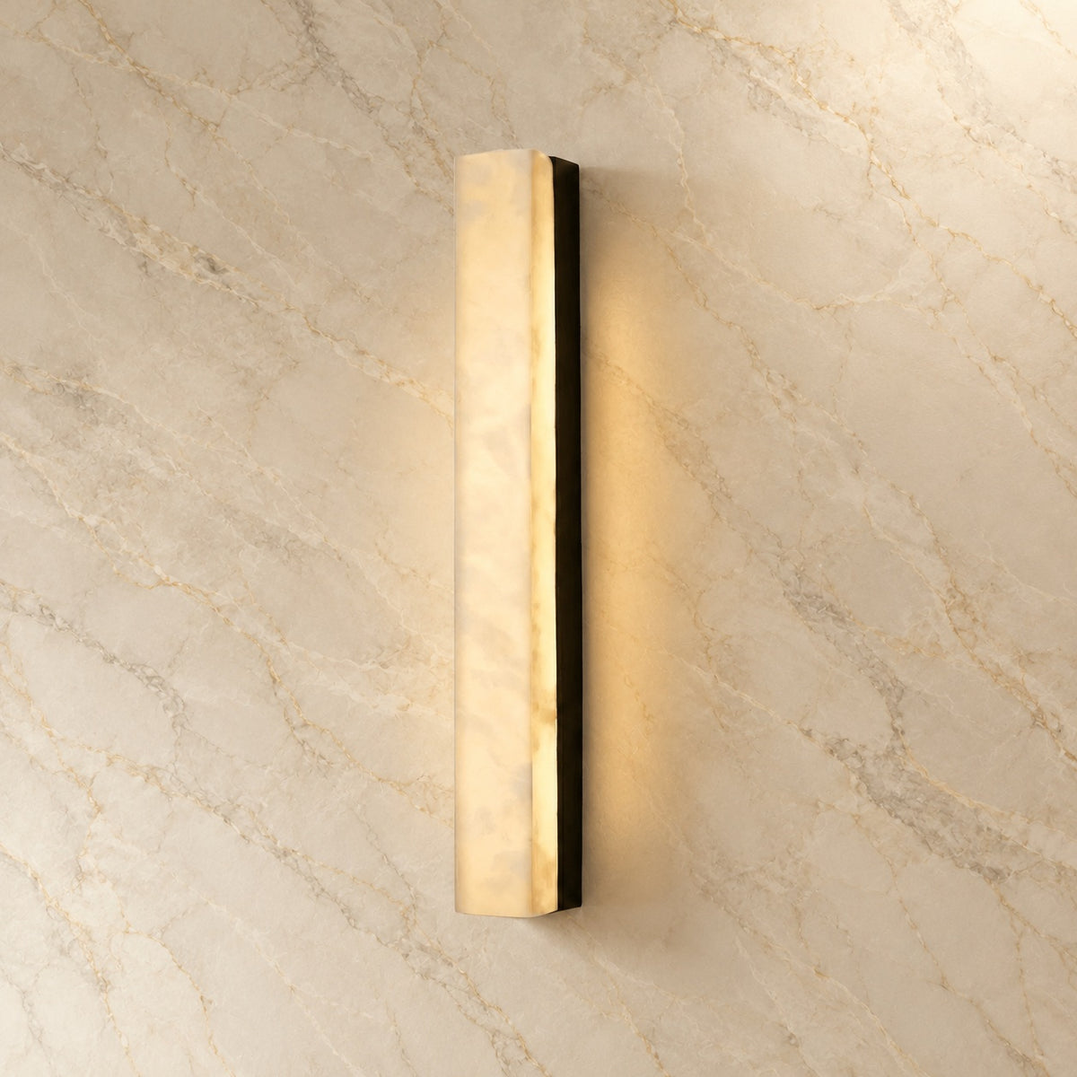 Dara Alabaster Linear Wall Sconce with black hardware, illuminated, on a marble wall | CARRA HOME