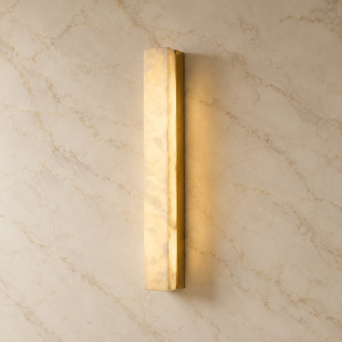 Dara Alabaster Linear Wall Sconce with gold hardware, illuminated, on a marble wall | CARRA HOME