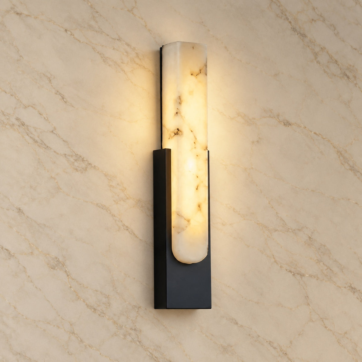 Emilia Alabaster Wall Sconce with black hardware, illuminated, on a marble wall | CARRA HOME