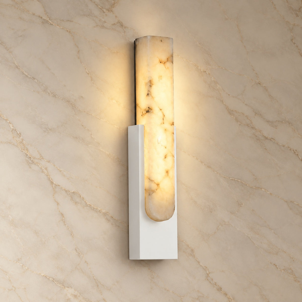 Emilia Alabaster Wall Sconce with white hardware, illuminated, on a marble wall | CARRA HOME