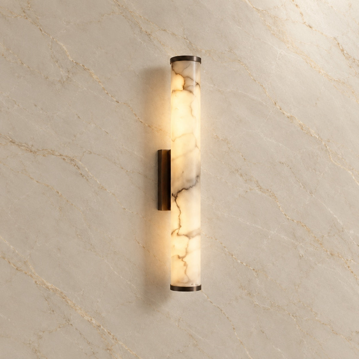 Falynis Alabaster Cylinder Wall Sconce with black hardware, illuminated, on a marble wall | CARRA HOME