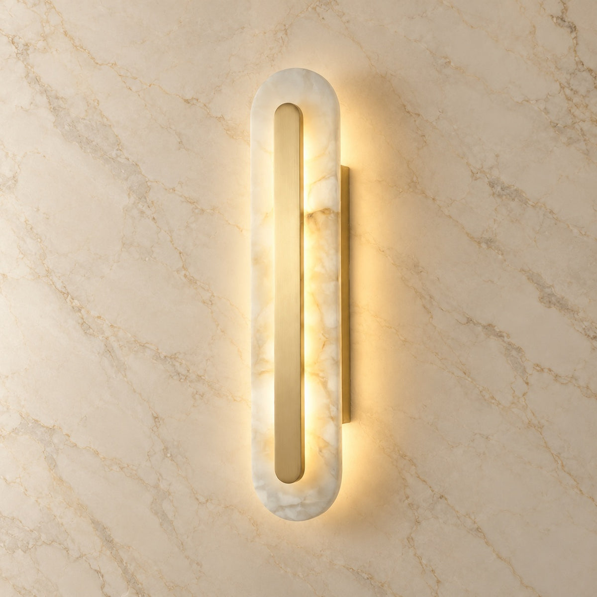 Lofos Alabaster Oval Wall Sconce with gold hardware, illuminated, on a marble wall | CARRA HOME