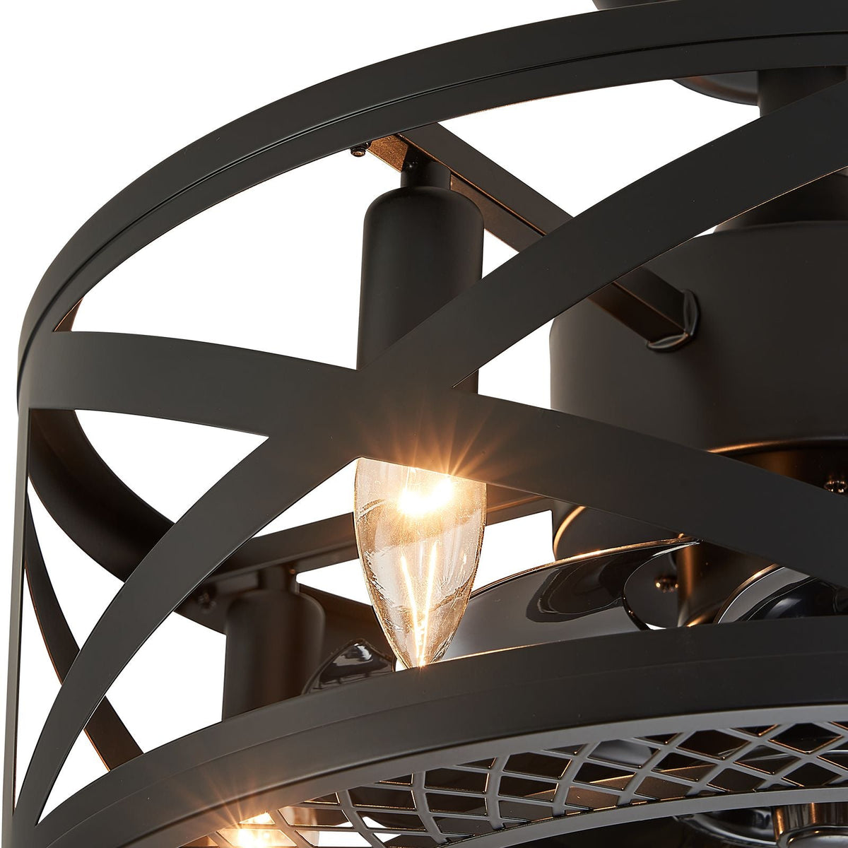 Close-up of industrial caged fan — vintage E12-style bulb glow, crisscross matte black metal frame, warm light reflection | CARRA HOME