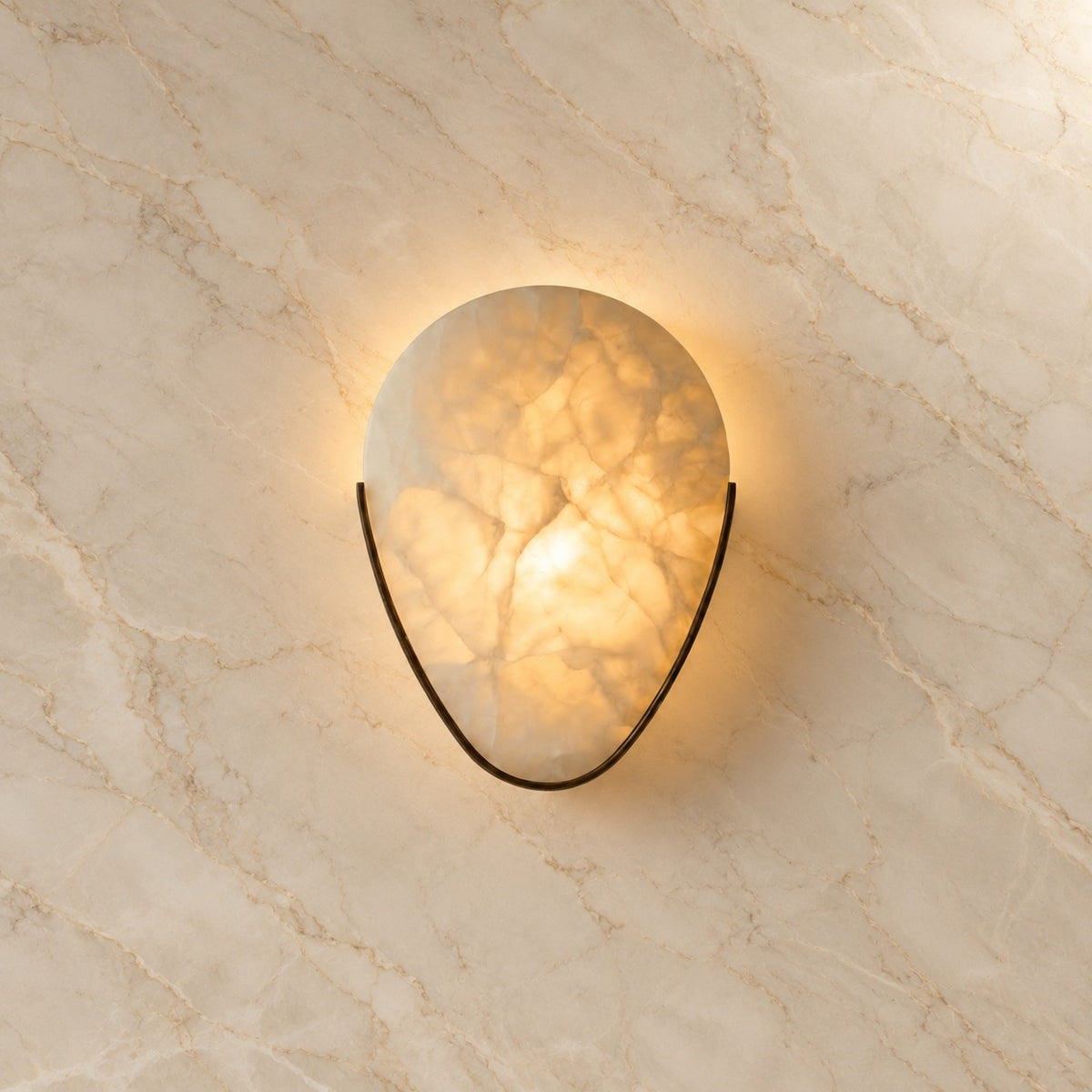 Ritu Alabaster Teardrop Wall Sconce with bronze hardware, illuminated, on a marble wall | CARRA HOME